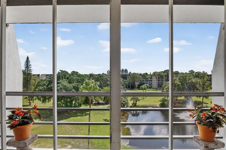 Expansive exterior scenery featuring a water body with a fountain, lush green landscaping, and mature trees