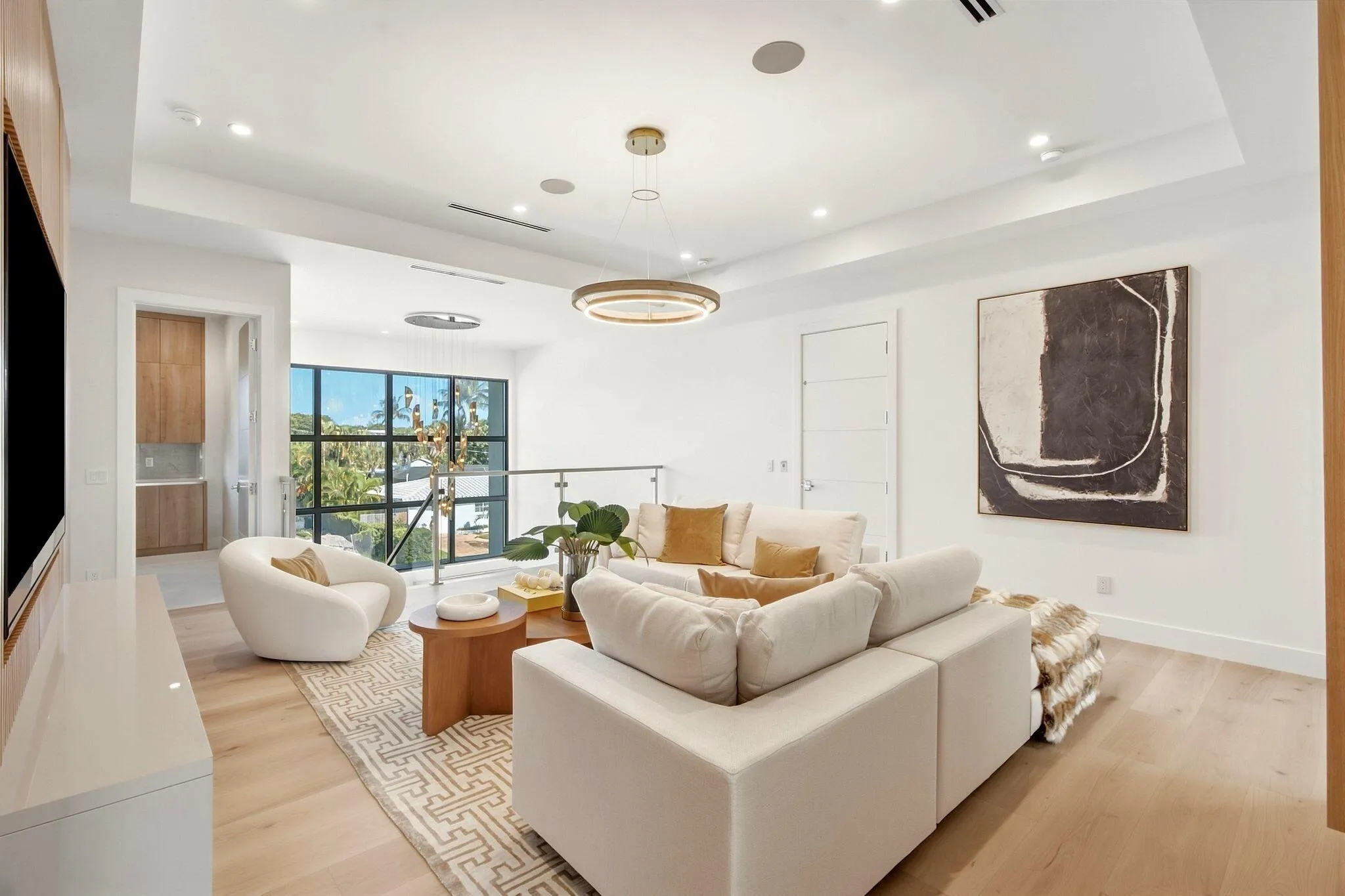 Spacious living area featuring light wood-finish flooring, a contemporary chandelier, recessed lighting, and a glass-paneled railing