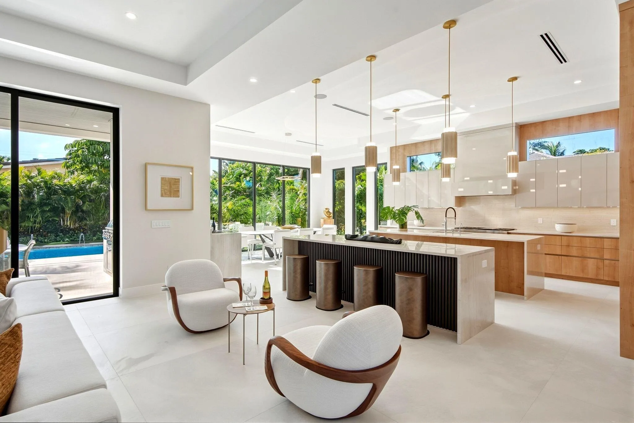 Modern kitchen featuring a large island with integrated seating, light wood-finish cabinetry, and contemporary pendant lighting