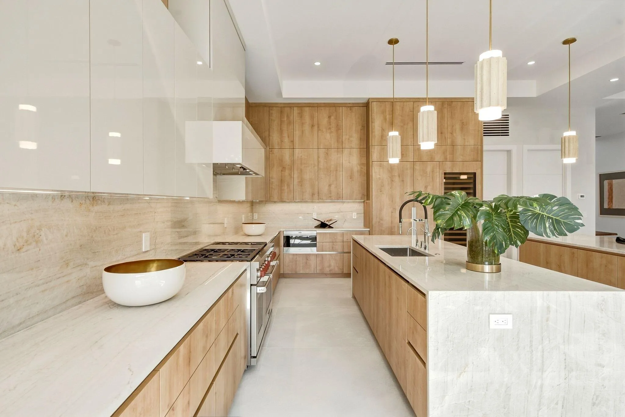 Gourmet kitchen with sleek white upper cabinetry, wood-finish lower cabinetry, stone countertops, integrated range, and an expansive island with a sink and modern pendant lighting