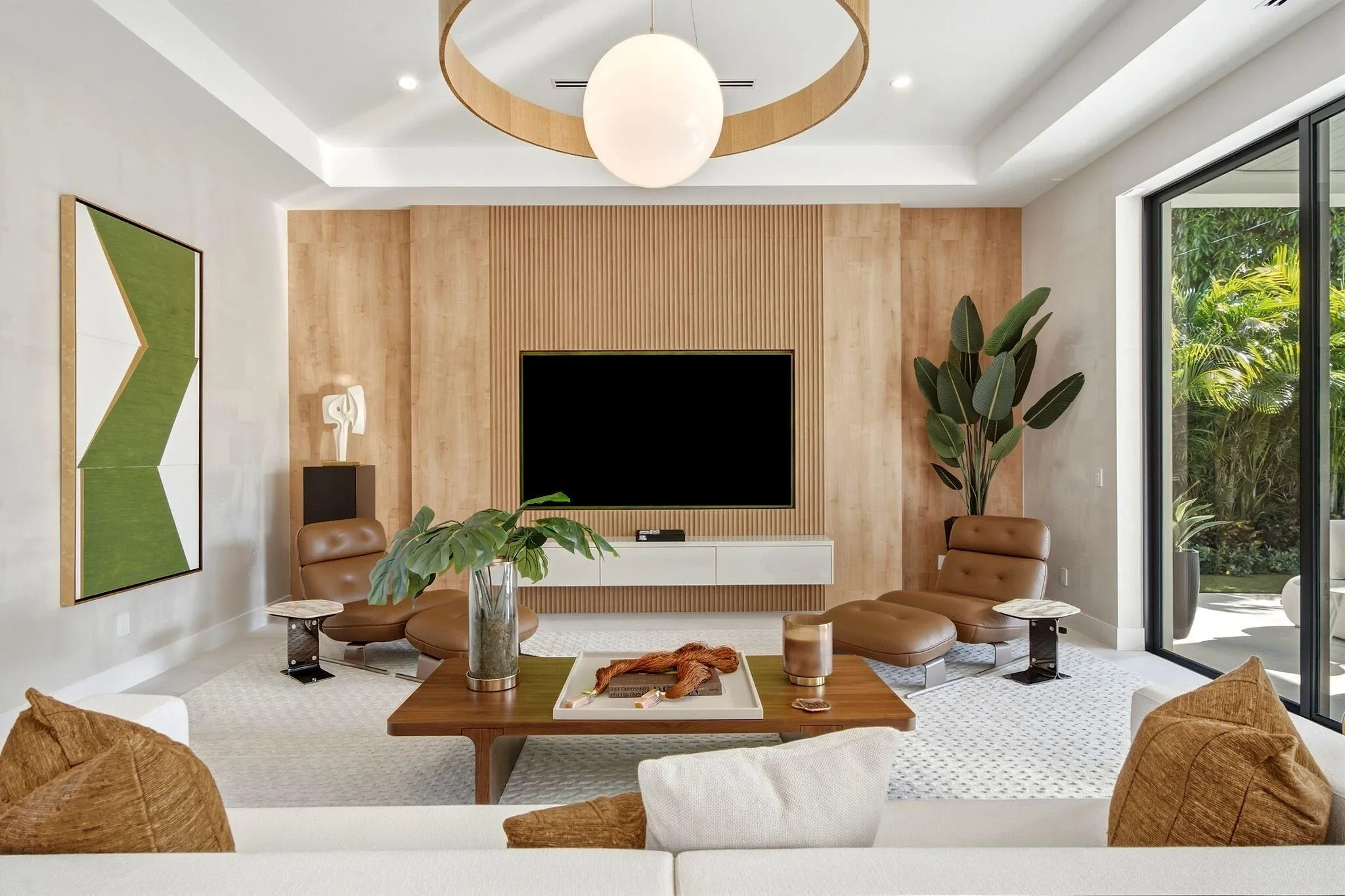 Spacious living area featuring a tray ceiling, a large built-in media wall with wood paneling and slatted accents, and wide glass sliding doors