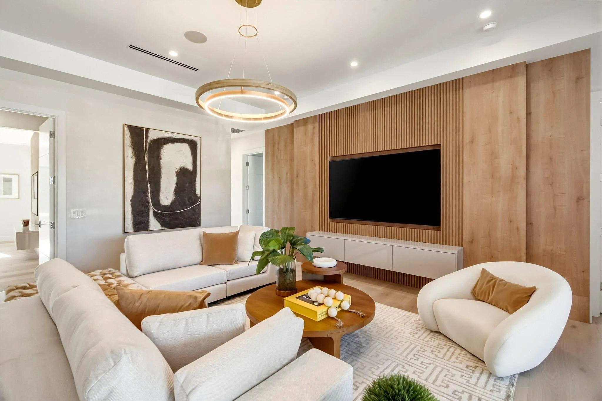 Textured wood-panel accent wall with integrated media console and built-in display, overhead recessed lighting, and a contemporary chandelier
