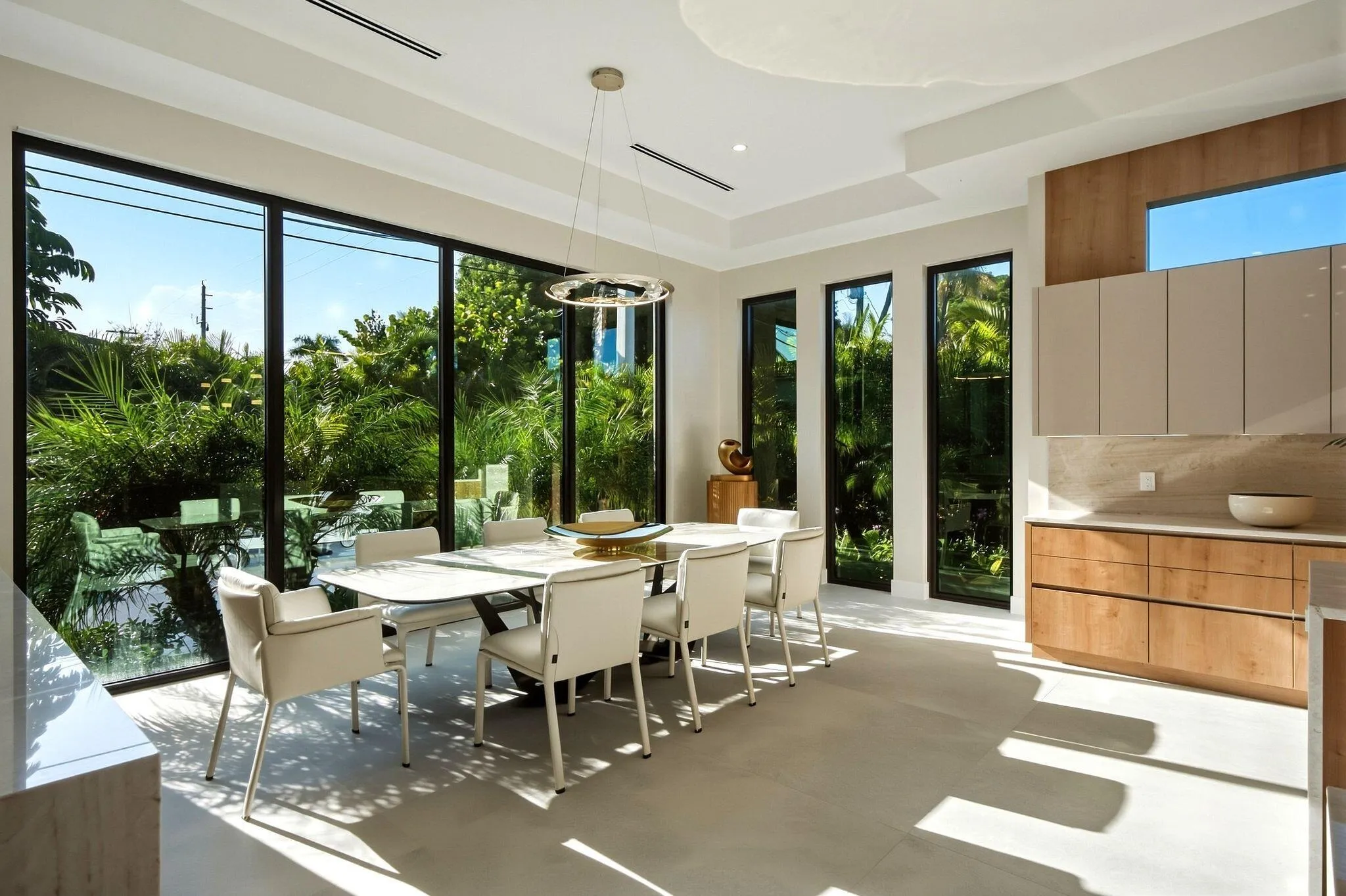 Floor-to-ceiling windows, recessed lighting, and a modern chandelier illuminate this dining space