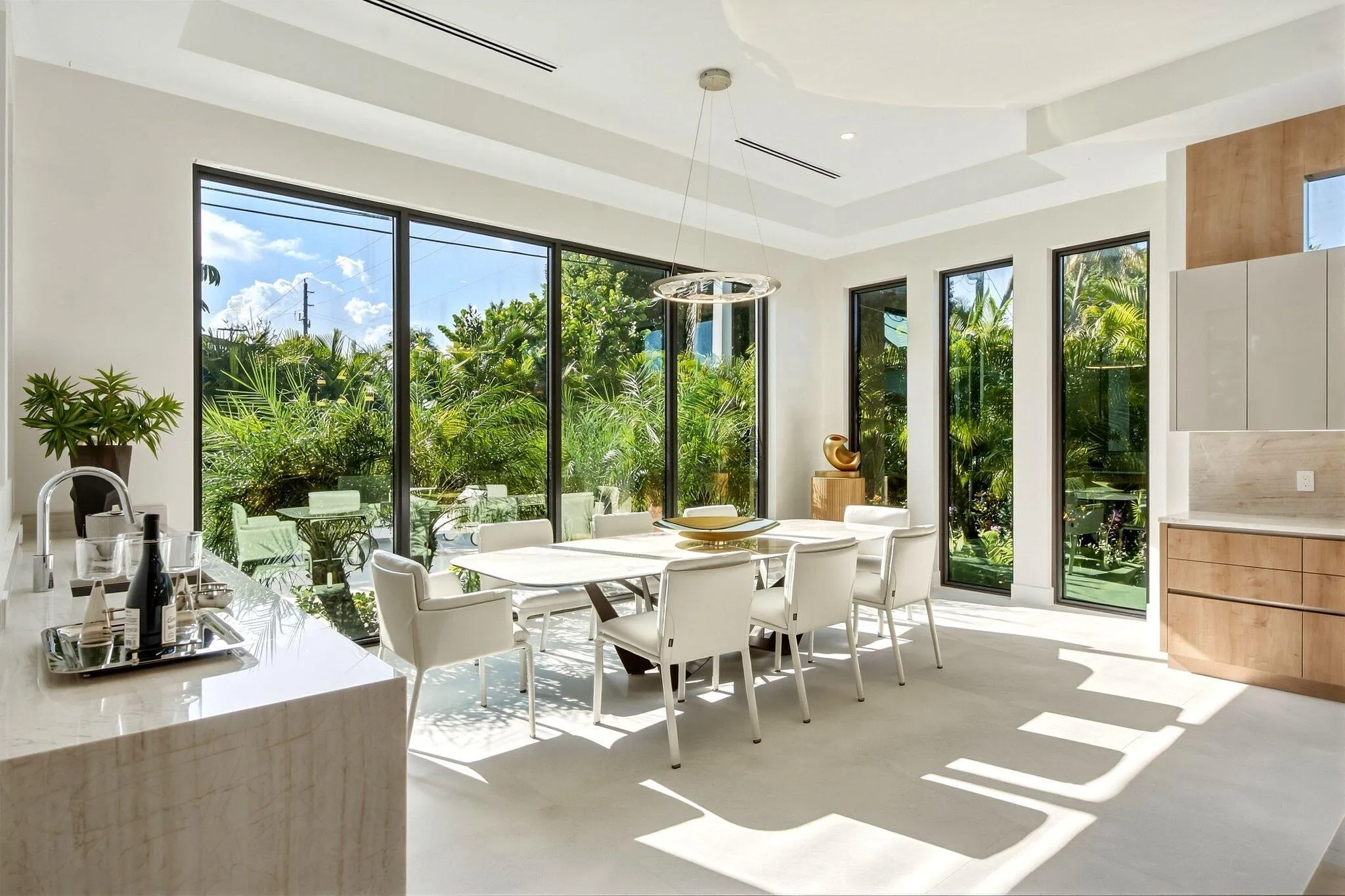 Expansive floor-to-ceiling windows, built-in light wood cabinetry, stone countertops, recessed lighting, and a contemporary chandelier