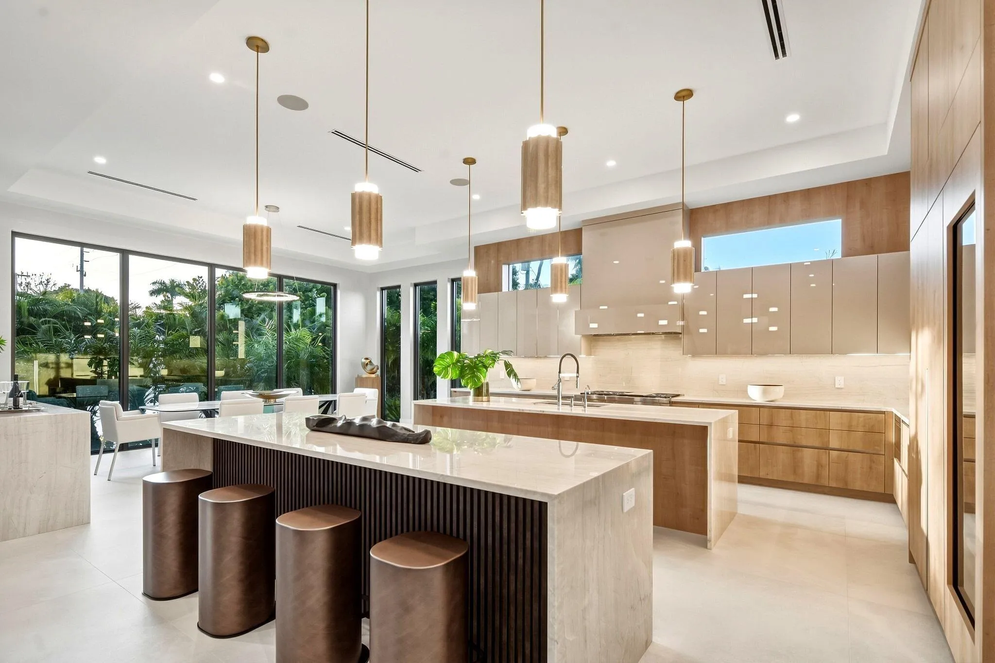 Gourmet kitchen with double islands, light wood-finish cabinetry, integrated appliances, and floor-to-ceiling windows