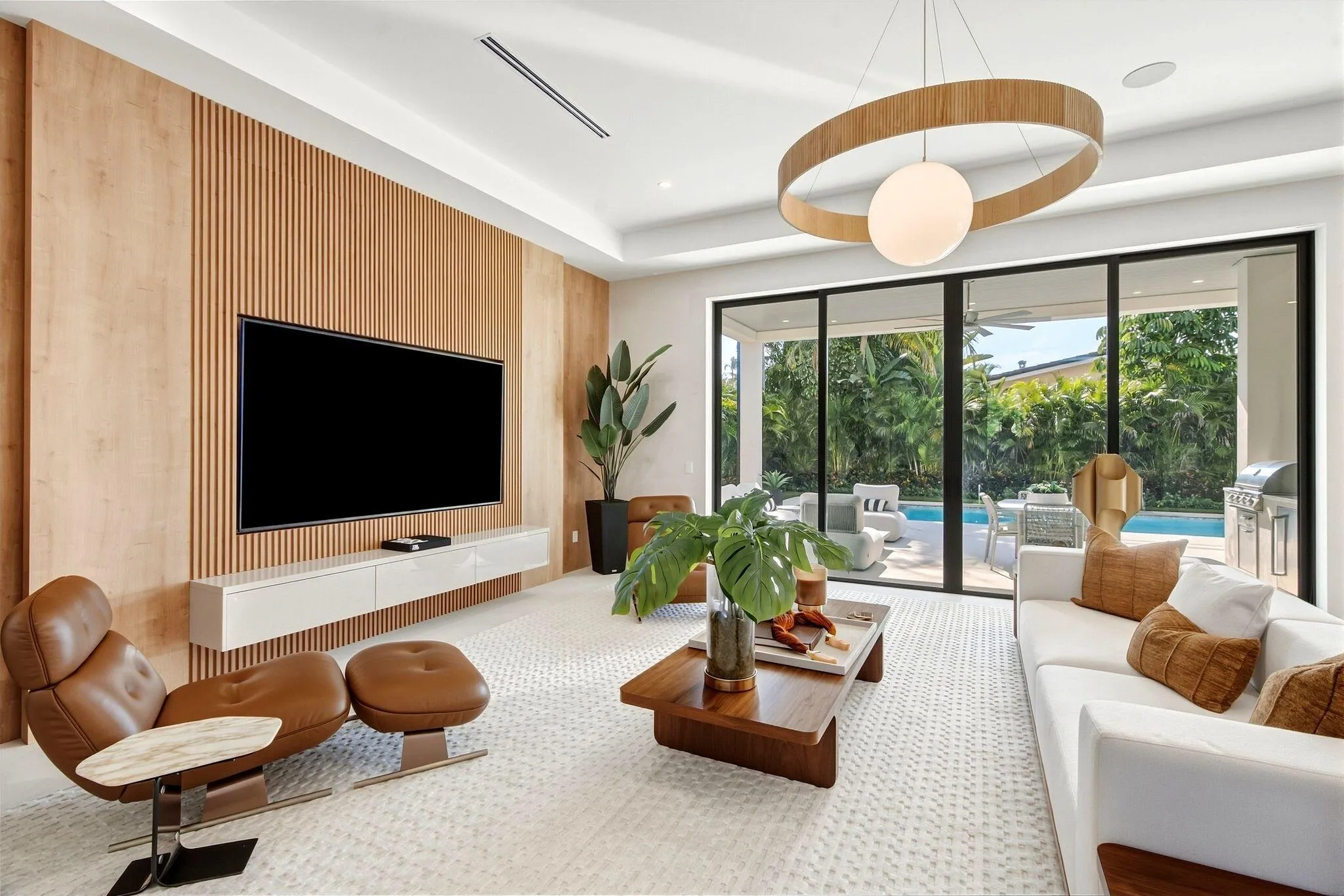 Wood slat accent wall, built-in entertainment console, recessed ceiling lighting, a contemporary chandelier, and sliding glass doors opening to outdoor living