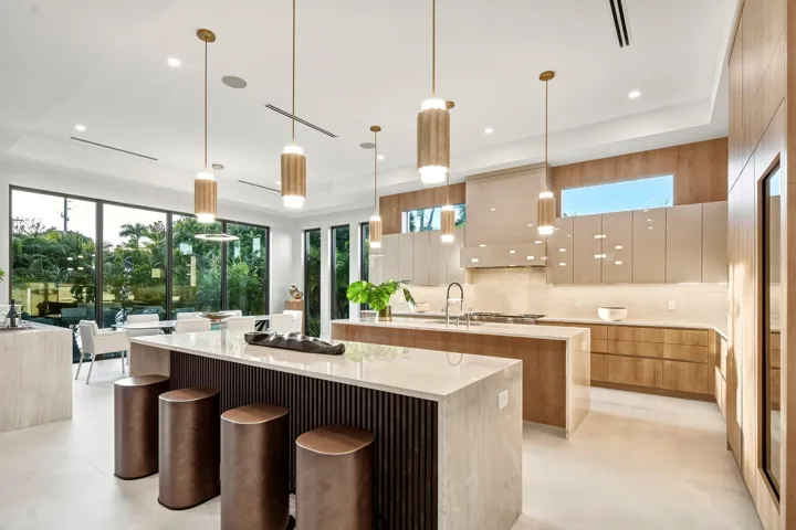 Gourmet kitchen with double islands, light wood-finish cabinetry, integrated appliances, and floor-to-ceiling windows