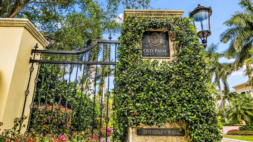 Ornate iron gate with decorative elements, stone columns, lush green foliage, and a prominent "Old Palm Golf Club" sign