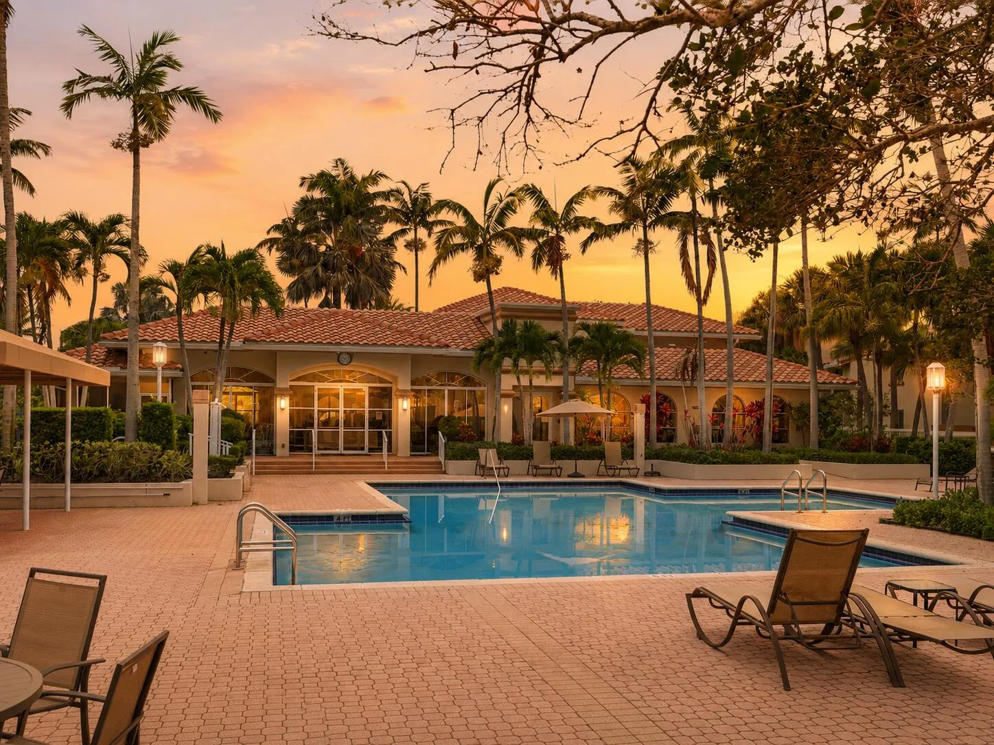 Resort-style South Florida pool at sunset with palm trees, lounge chairs, and a warm golden sky.