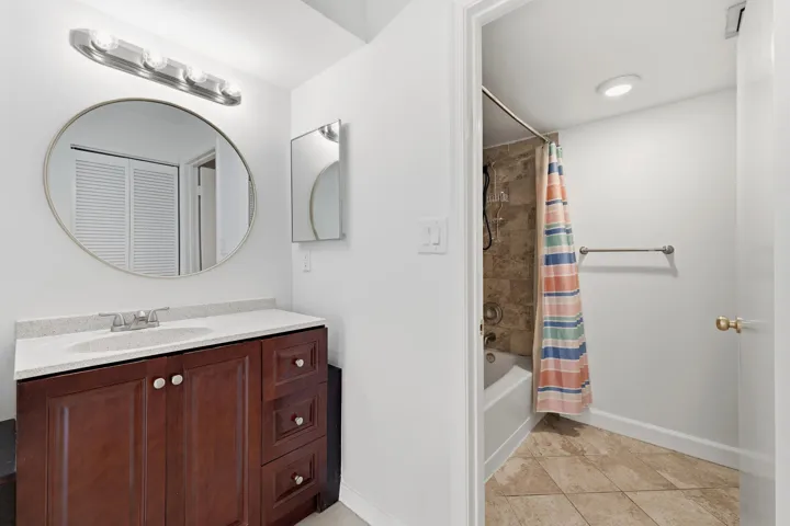 Bathroom featuring a dark wood-finish vanity with a light countertop, an oval mirror, and a four-bulb vanity light fixture