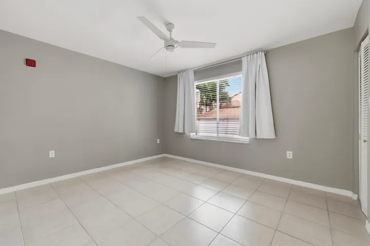 Bedroom two featuring neutral gray walls, beige tile flooring, and a white ceiling fan