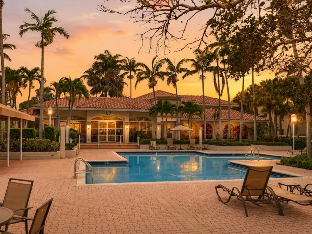 Resort-style South Florida pool at sunset with palm trees, lounge chairs, and a warm golden sky.