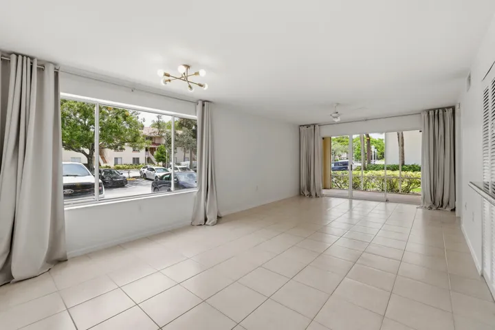 Spacious living area featuring neutral tile flooring, a wide window with light-filtering drapes, and a contemporary ceiling fixture
