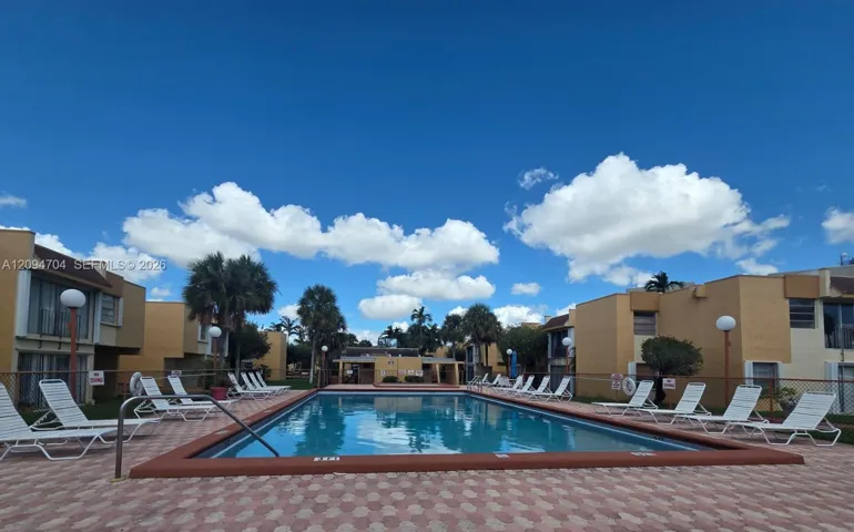 In-ground swimming pool featuring a concrete coping border, paver deck, and surrounding metal fencing