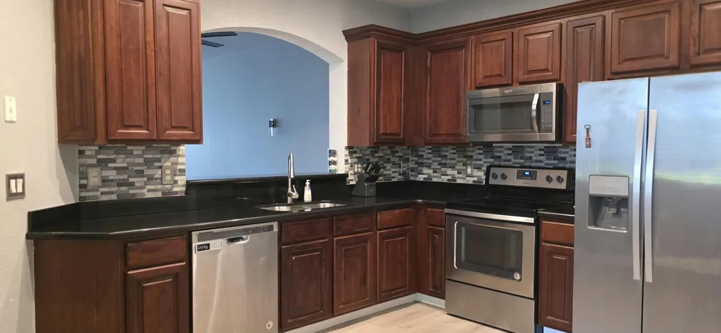 Kitchen featuring wood cabinetry, dark countertops, a mosaic tile backsplash, and stainless steel appliances