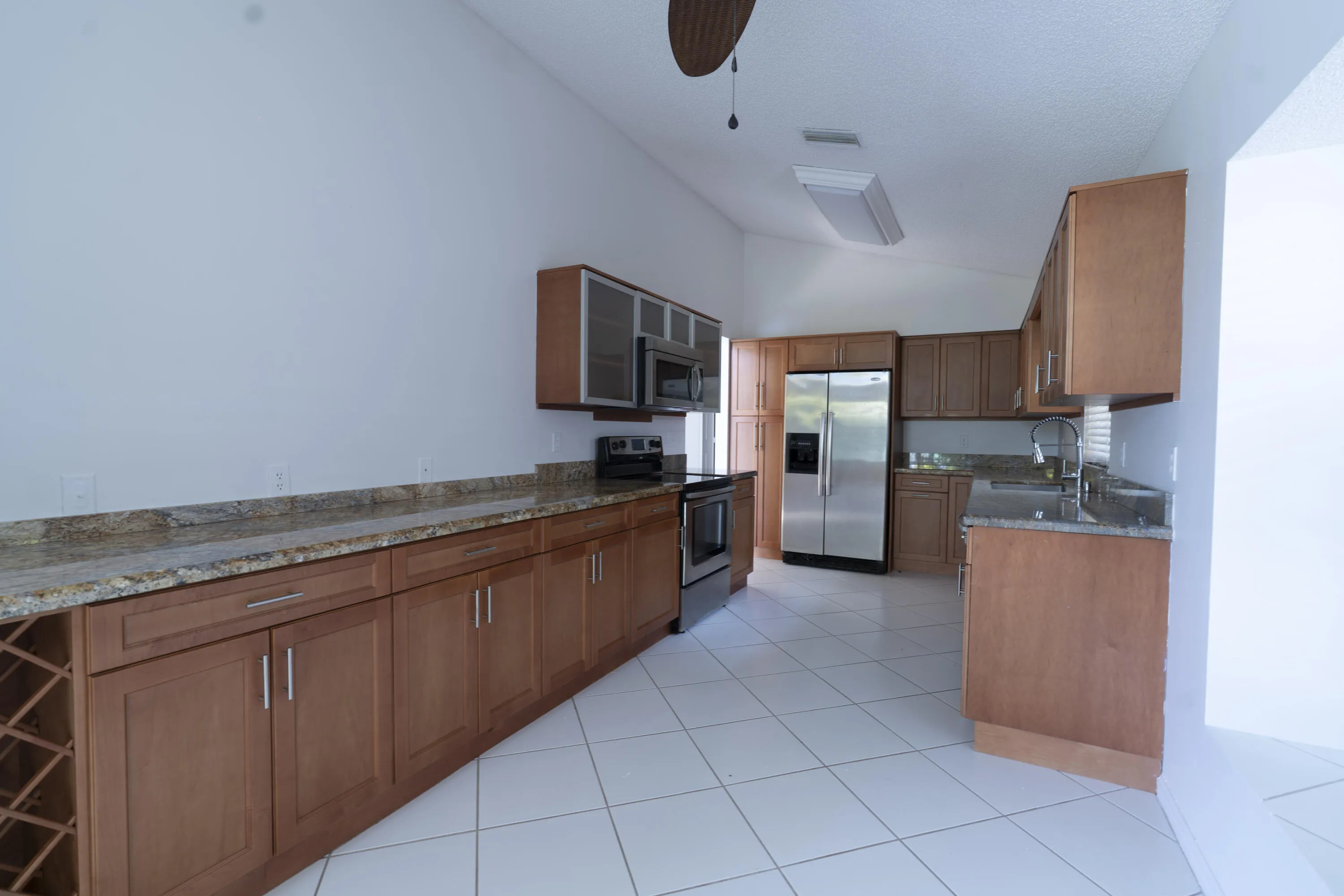 Kitchen featuring vaulted ceilings, white tile flooring, wood cabinetry with brushed nickel hardware, and stainless steel appliances