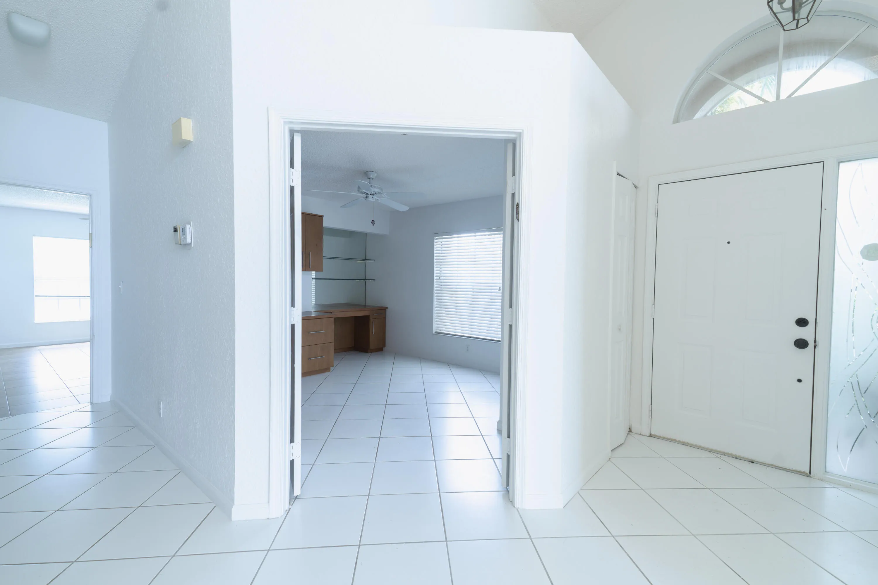 White tile flooring, vaulted ceiling, arched transom window, built-in desk with shelving, and ceiling fan