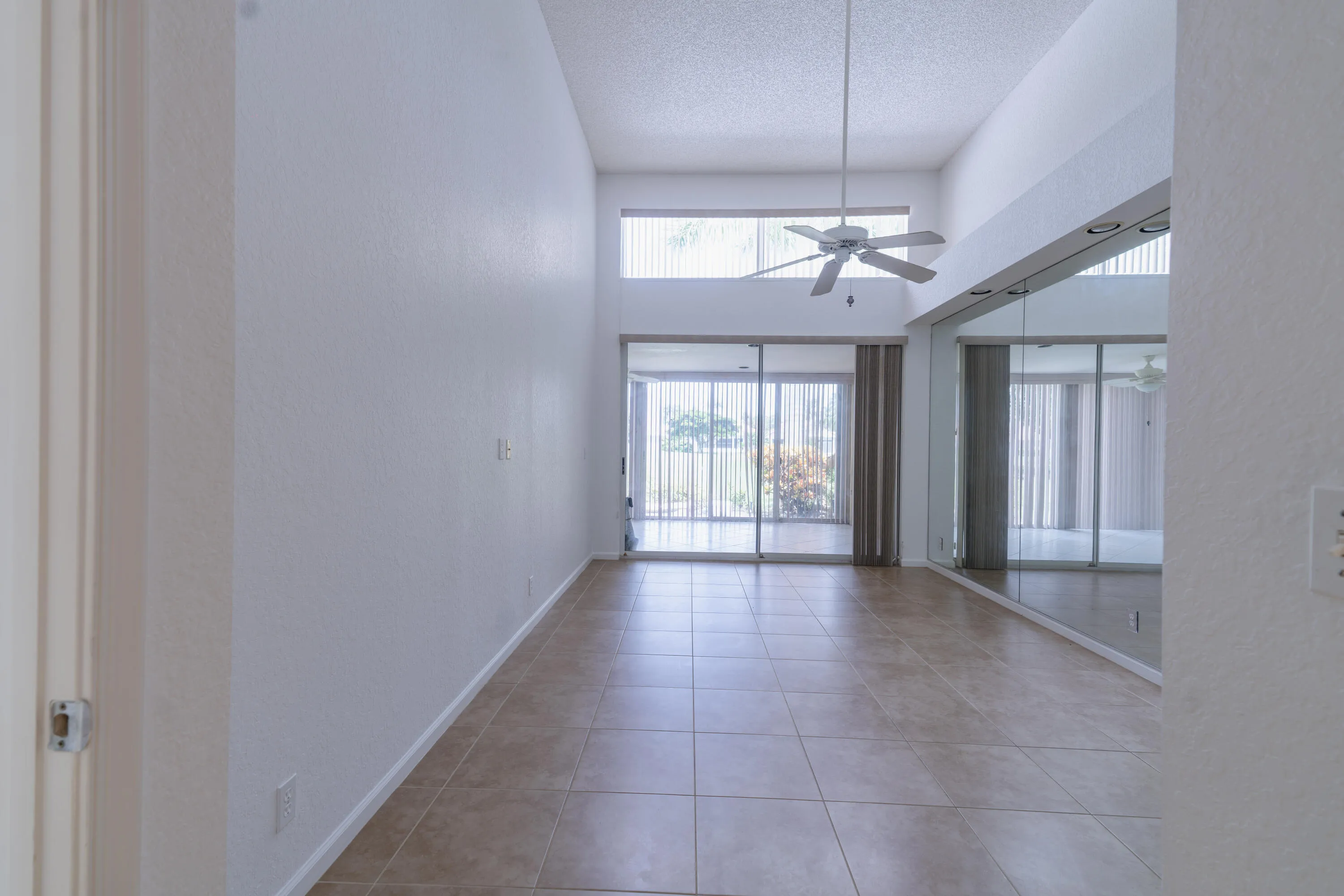 Vaulted ceilings with a ceiling fan, full-height mirrored wall, large format tile flooring, and sliding glass doors
