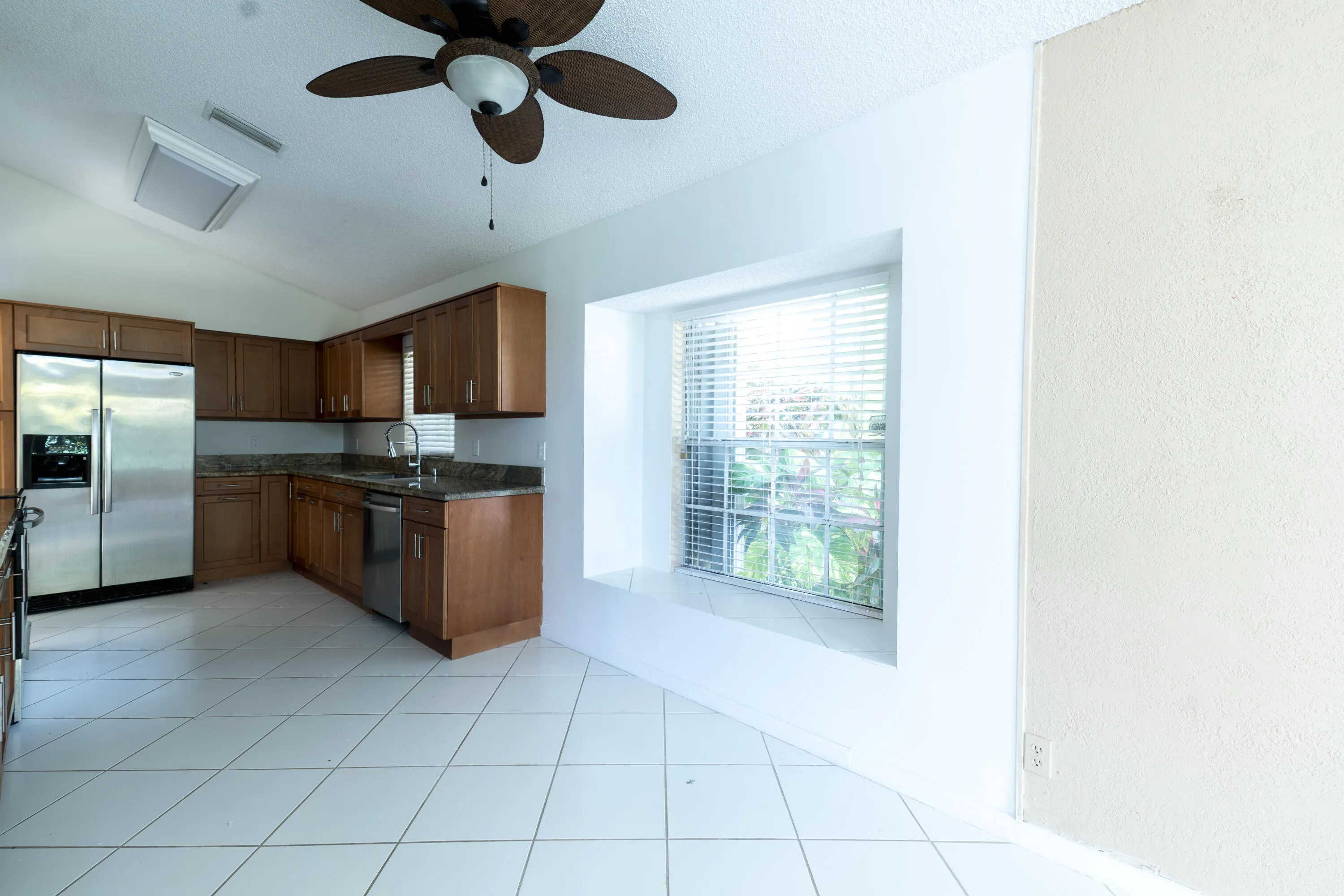 Kitchen with L-shaped wood cabinetry, stainless steel appliances, and a window with blinds