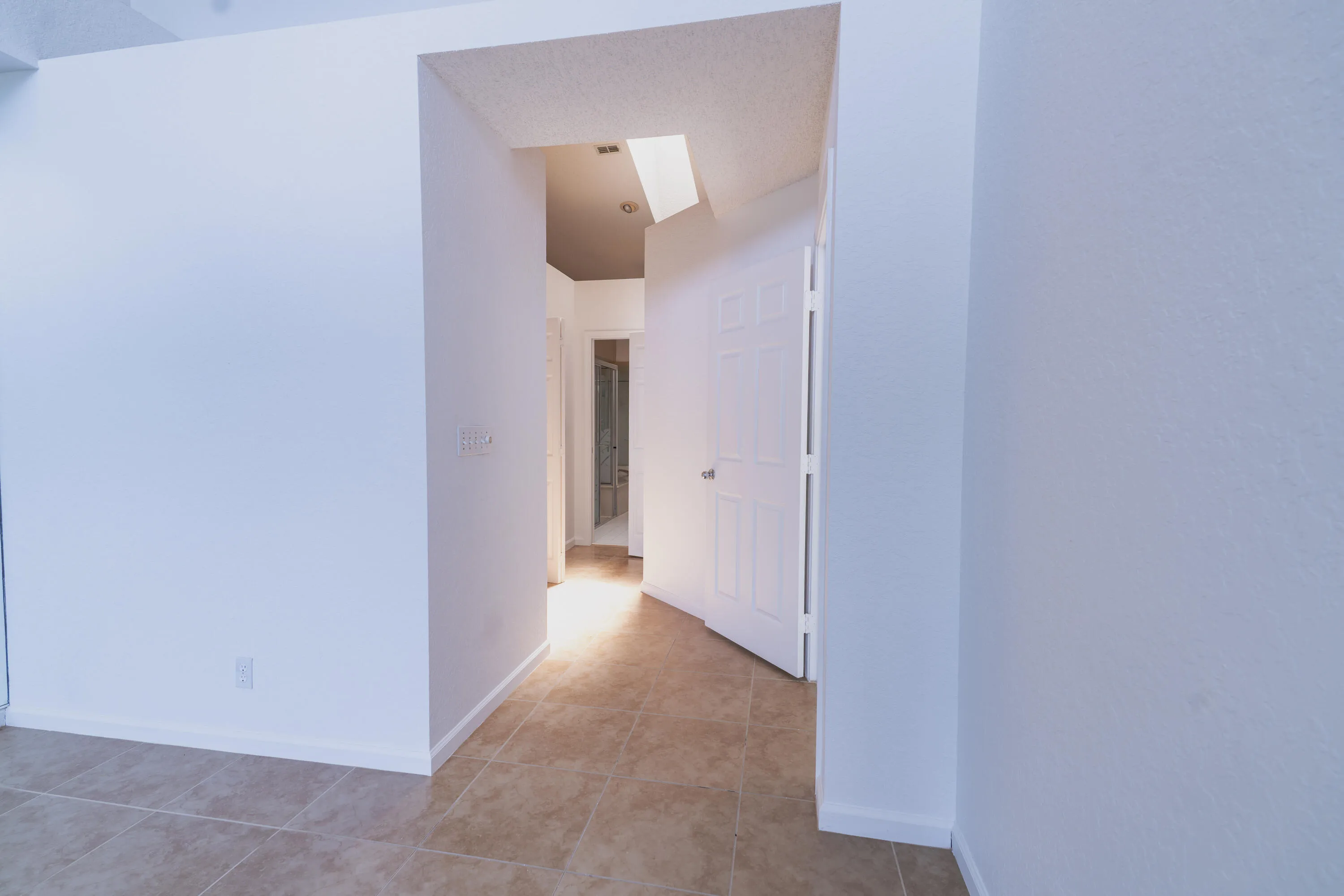 Recessed lighting illuminating a hallway with tile flooring and a paneled interior door