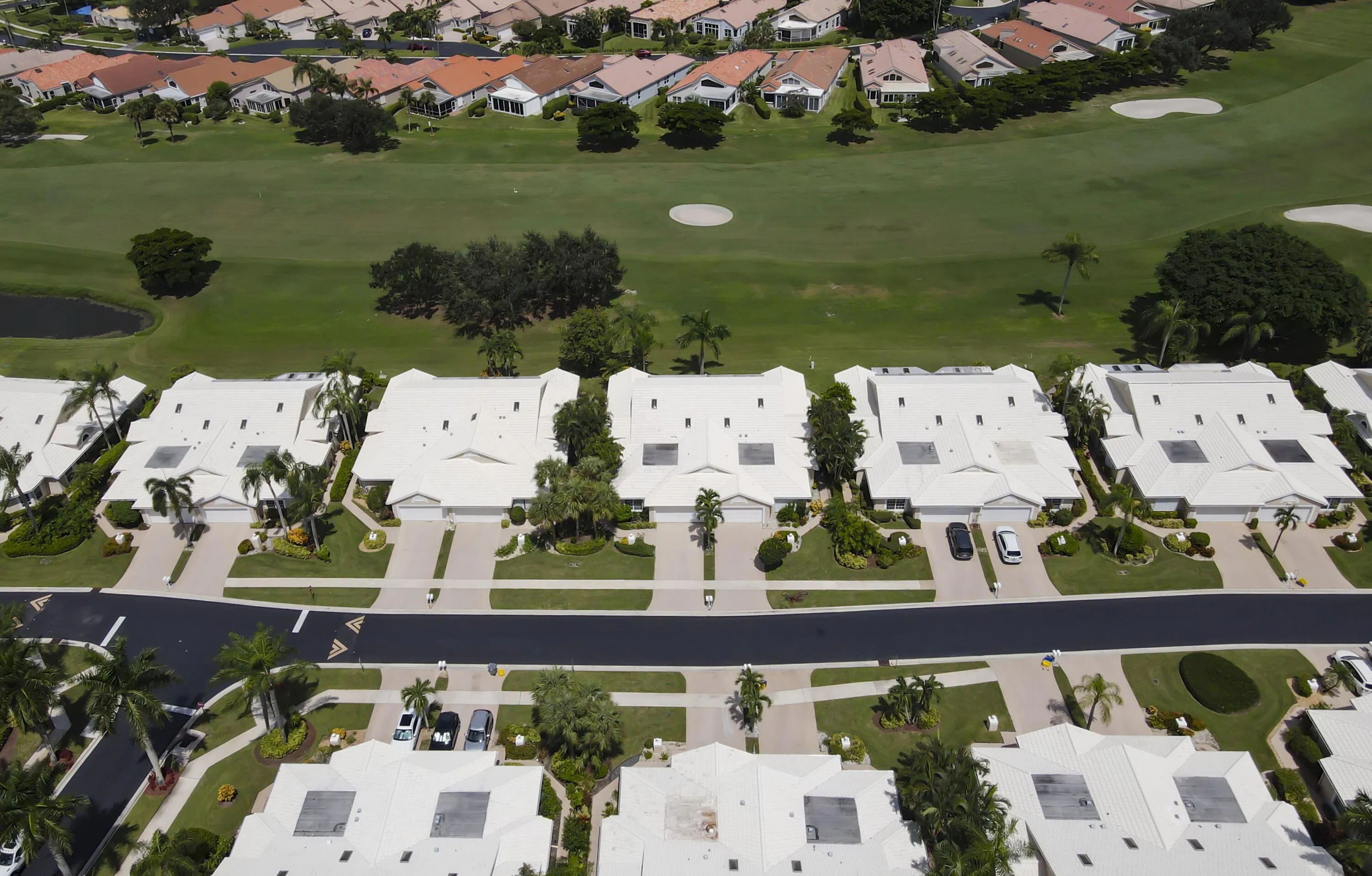Aerial perspective showcasing properties with white roofs and attached garages, bordered by a golf course and a paved road