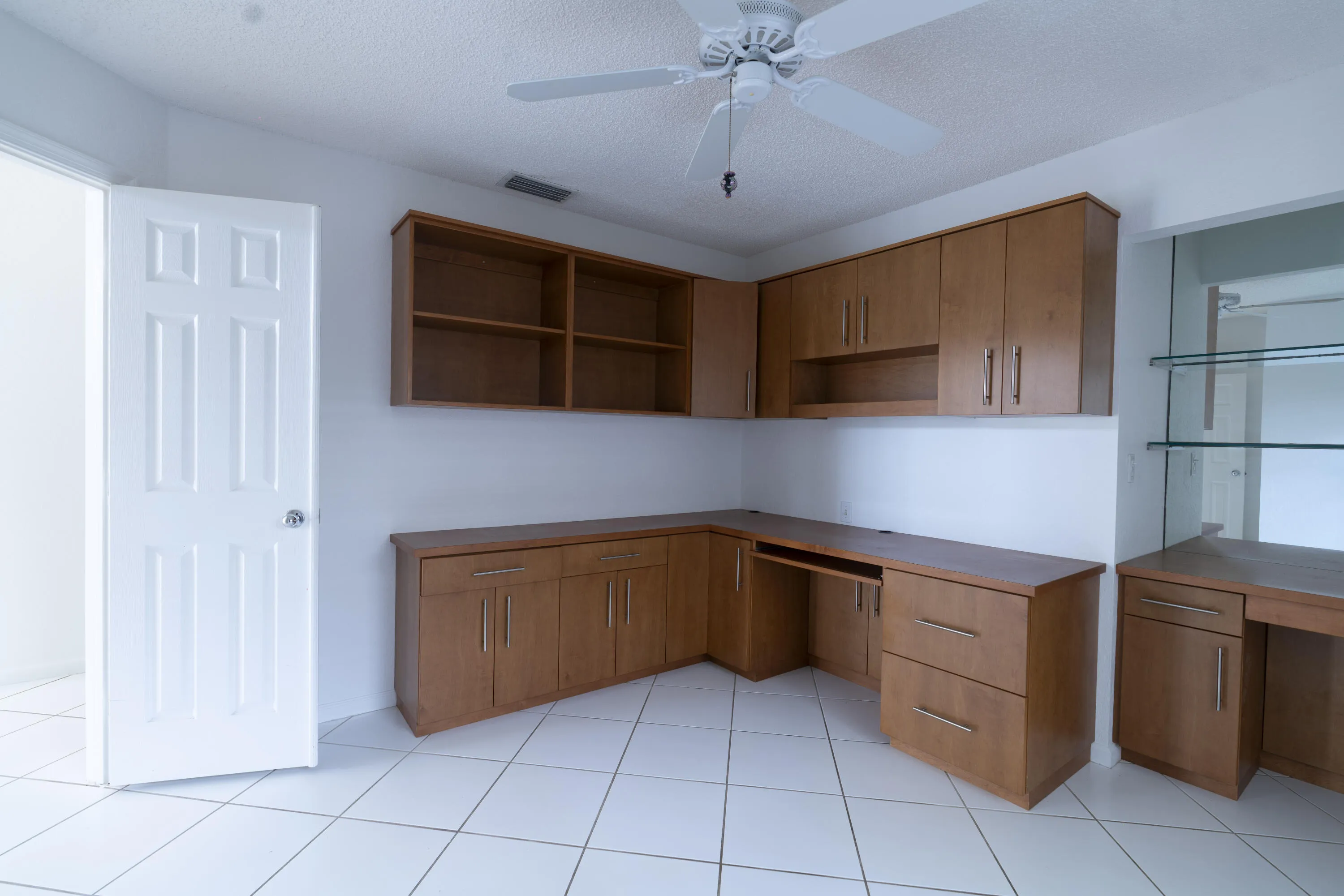 Built-in wood-finish cabinetry, integrated desk space, overhead shelving, and a ceiling fan