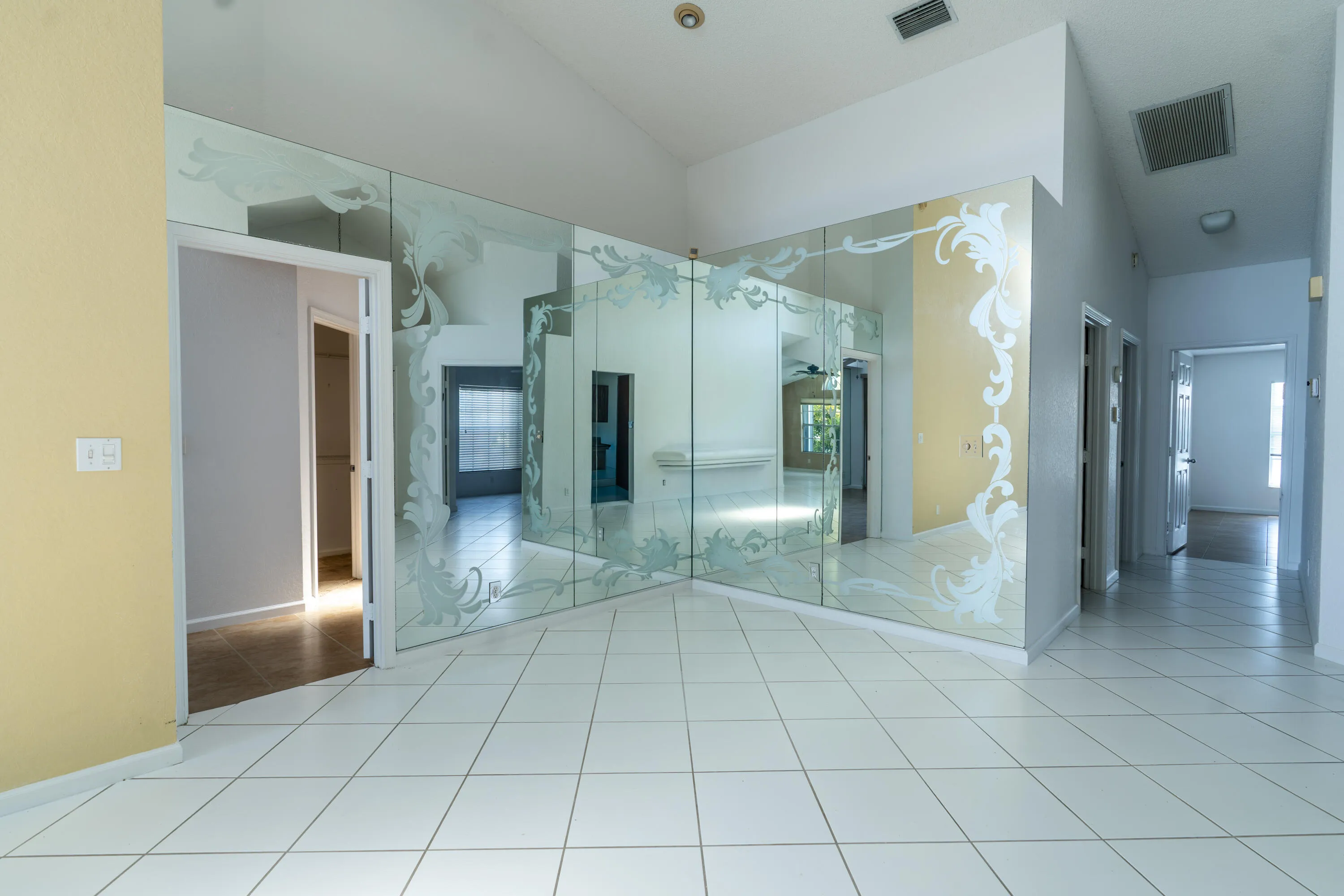 White tile flooring throughout, mirrored wall with etched design, vaulted ceiling, and recessed lighting