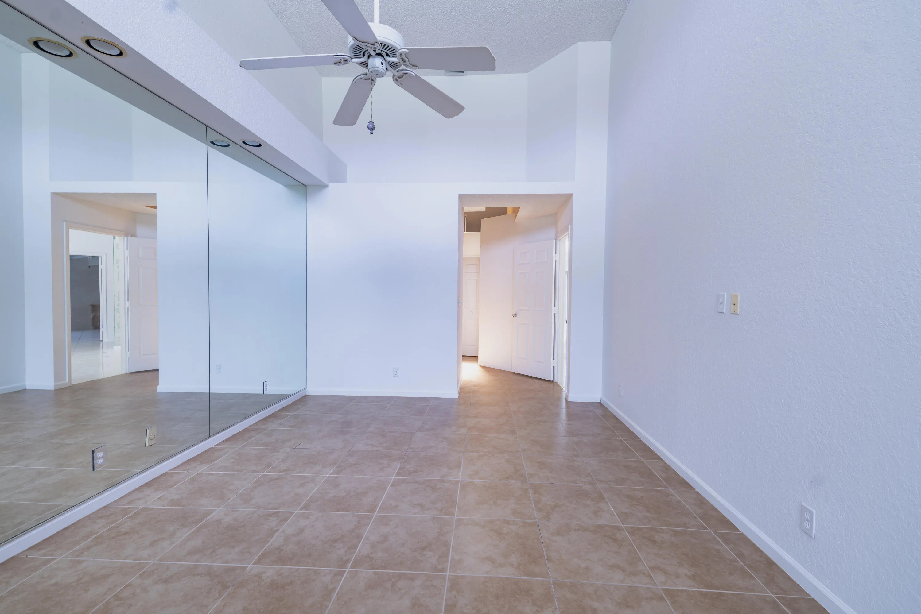 Vaulted ceiling with a ceiling fan, recessed lighting, mirrored wall, and tile flooring