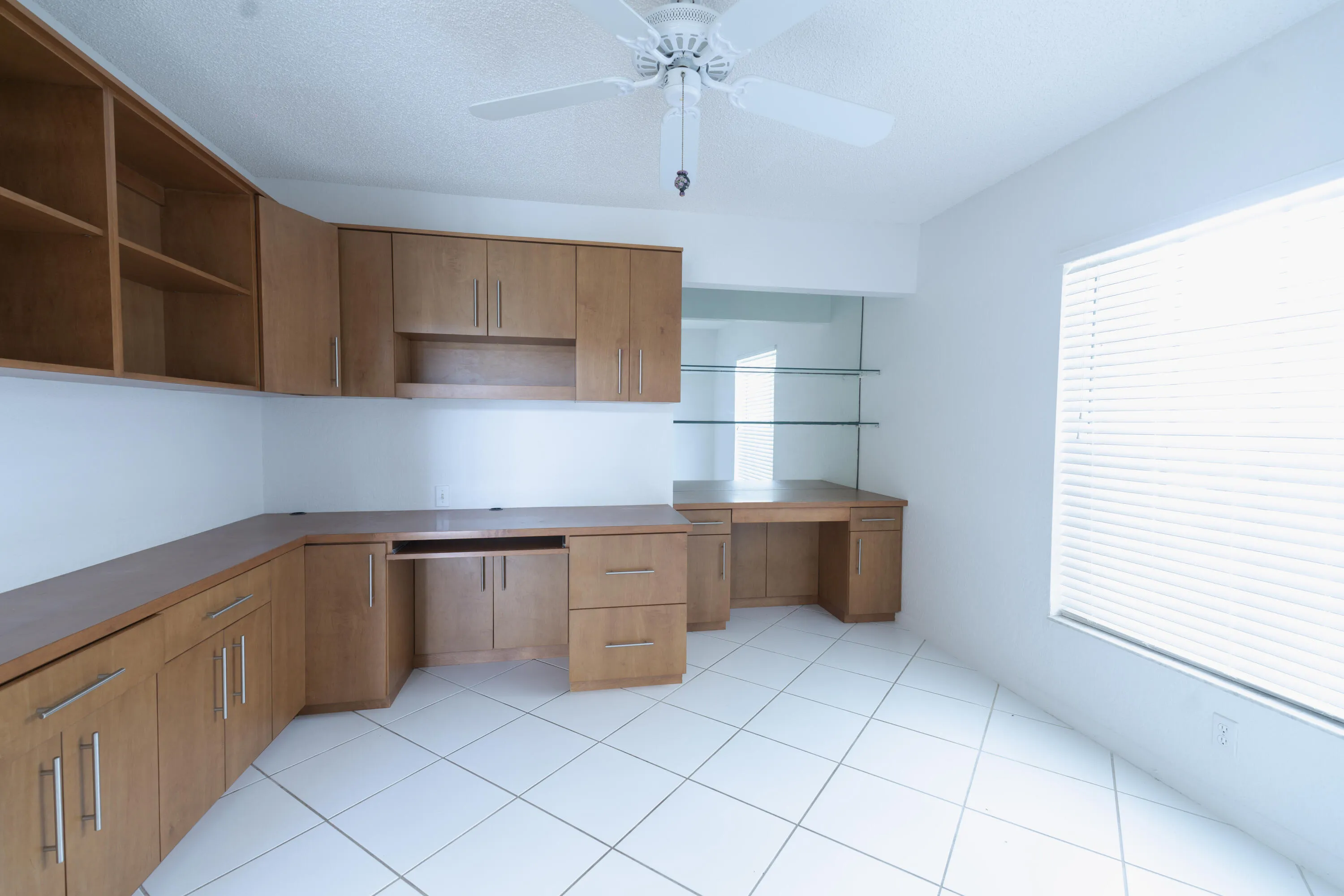 Integrated wood-finish cabinetry and desk system with open shelving and glass display shelves