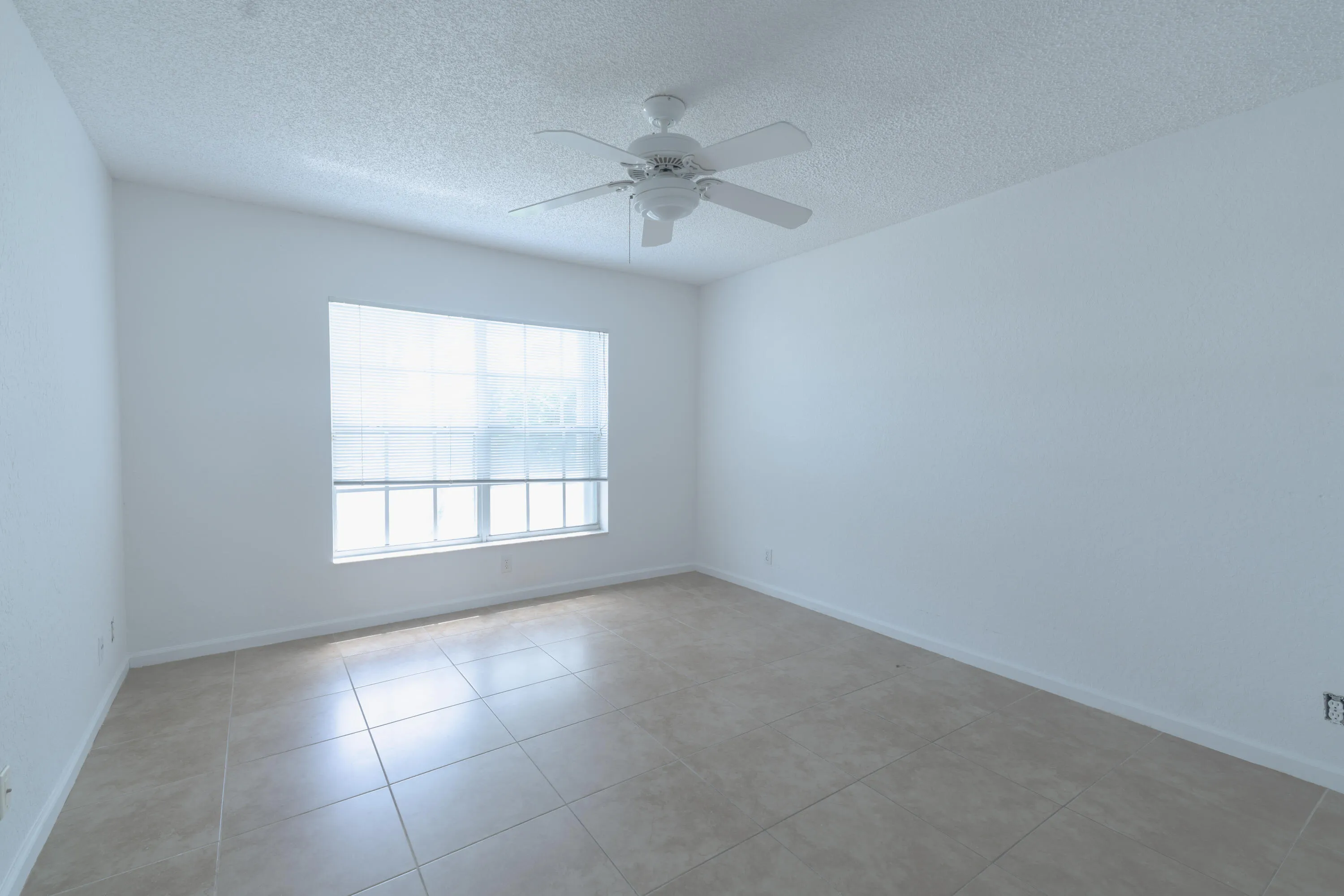 Bright interior with a window featuring horizontal blinds, overhead ceiling fan, white textured walls, and large format tile flooring