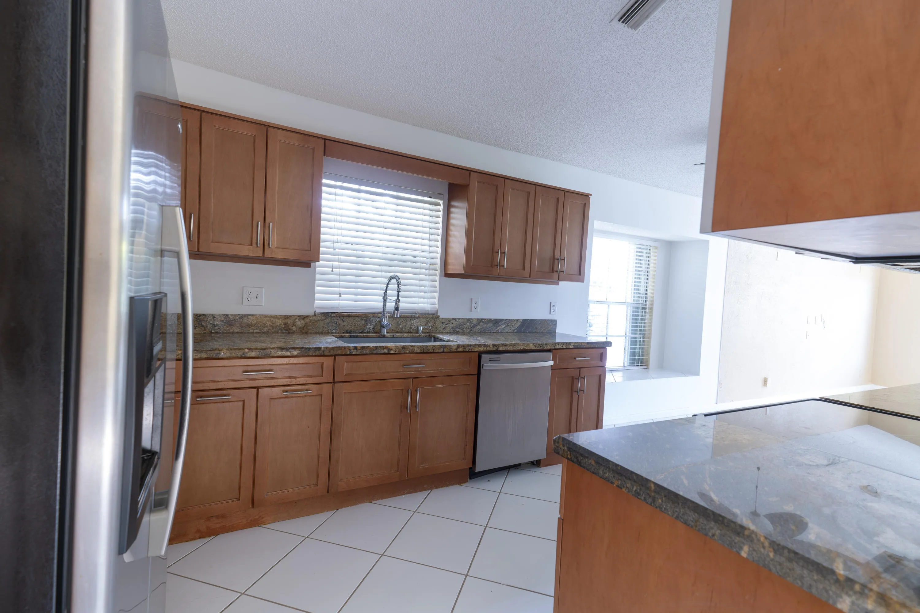 Kitchen featuring wood cabinetry, granite countertops, stainless steel appliances, and white tile flooring