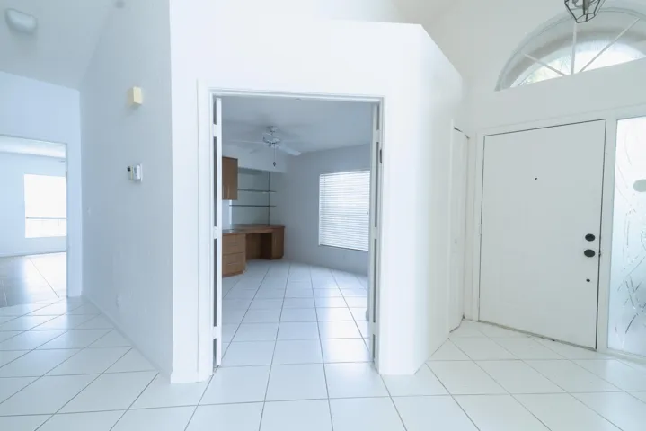 White tile flooring, vaulted ceiling, arched transom window, built-in desk with shelving, and ceiling fan