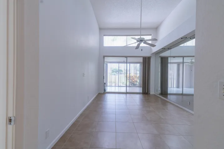 Vaulted ceilings with a ceiling fan, full-height mirrored wall, large format tile flooring, and sliding glass doors