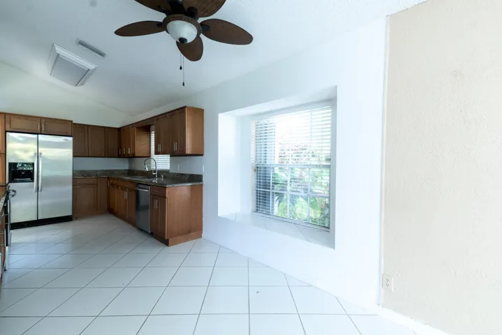 Kitchen with L-shaped wood cabinetry, stainless steel appliances, and a window with blinds