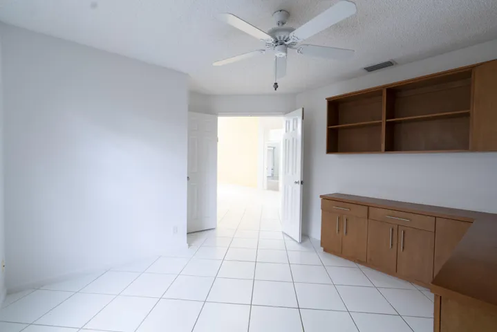 White tile flooring throughout, built-in wooden cabinetry with multiple shelves, and a ceiling fan with light fixture