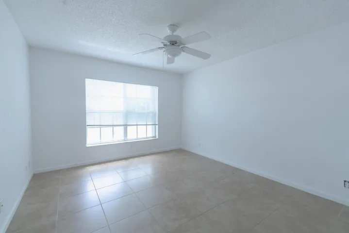 Bright interior with a window featuring horizontal blinds, overhead ceiling fan, white textured walls, and large format tile flooring