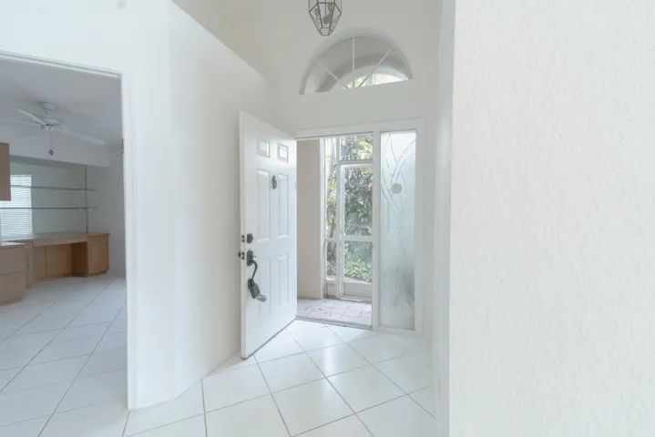 Entryway featuring white square tile flooring, a paneled entry door with sidelight, and an arched transom window