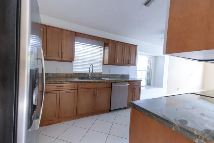 Kitchen featuring wood cabinetry, granite countertops, stainless steel appliances, and white tile flooring