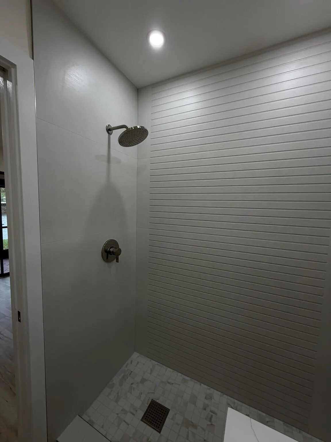 Recessed ceiling lighting, rain shower head, brushed nickel fixtures, horizontal textured wall tiling, and mosaic tile flooring