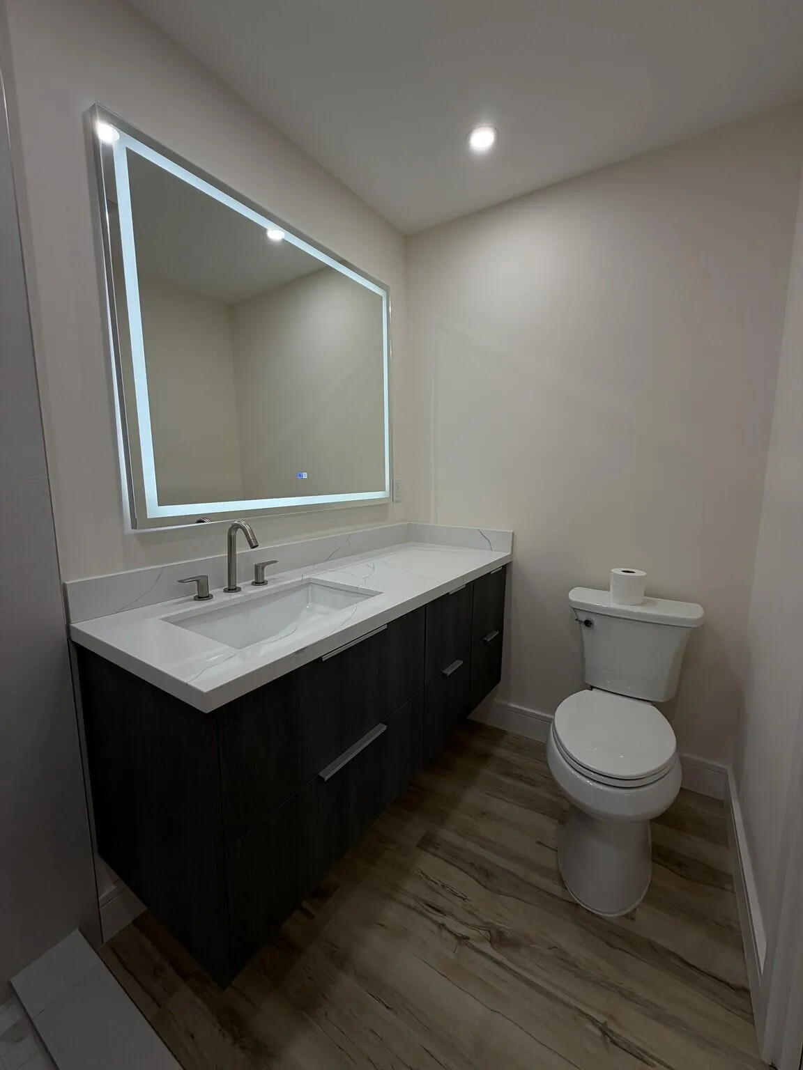 Floating vanity with an integrated sink, quartz countertop, and wood-finish flooring