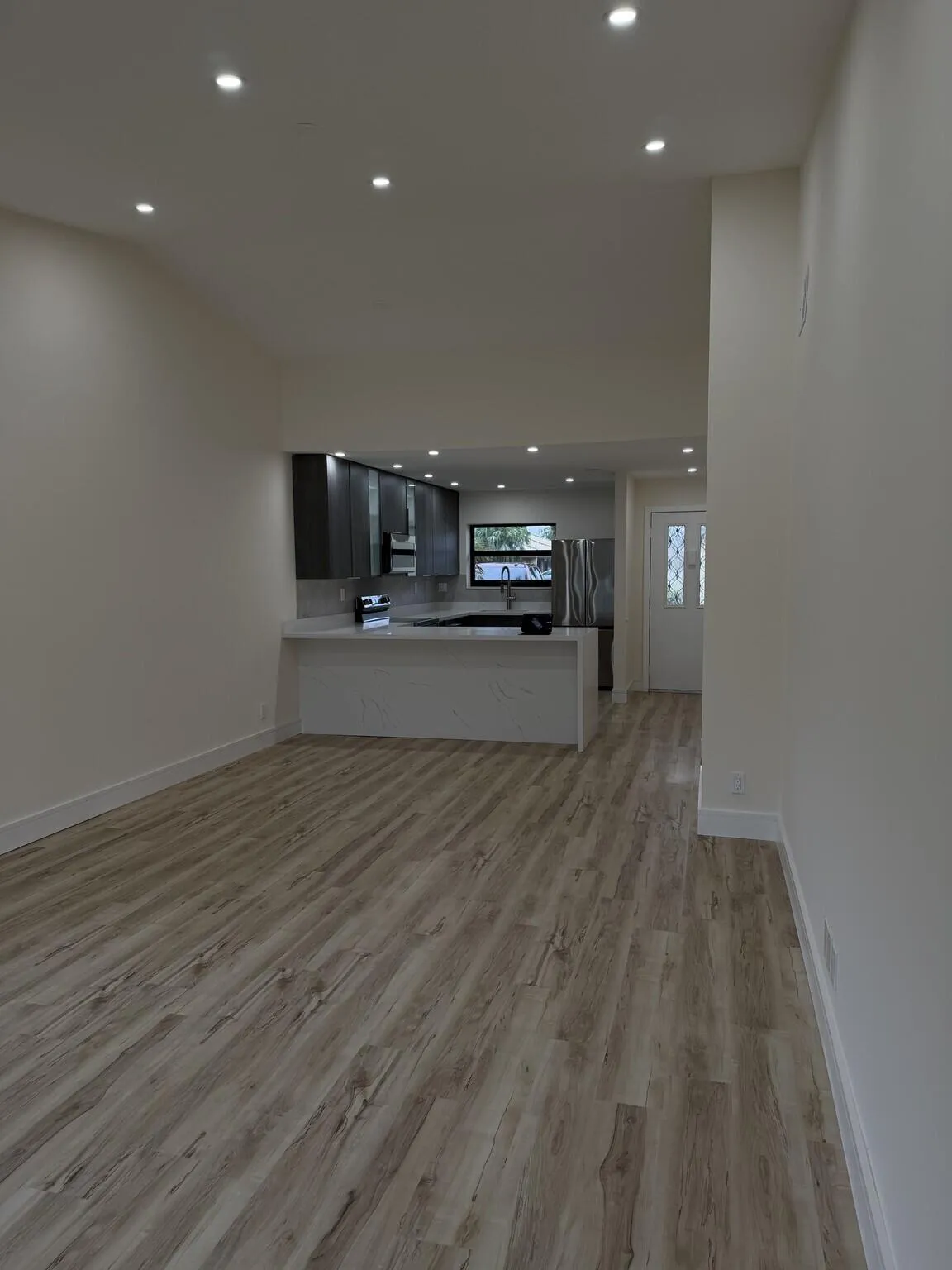 Recessed lighting, wood-finish flooring, a kitchen island with seating, dark wood-finish cabinetry, and stainless steel appliances