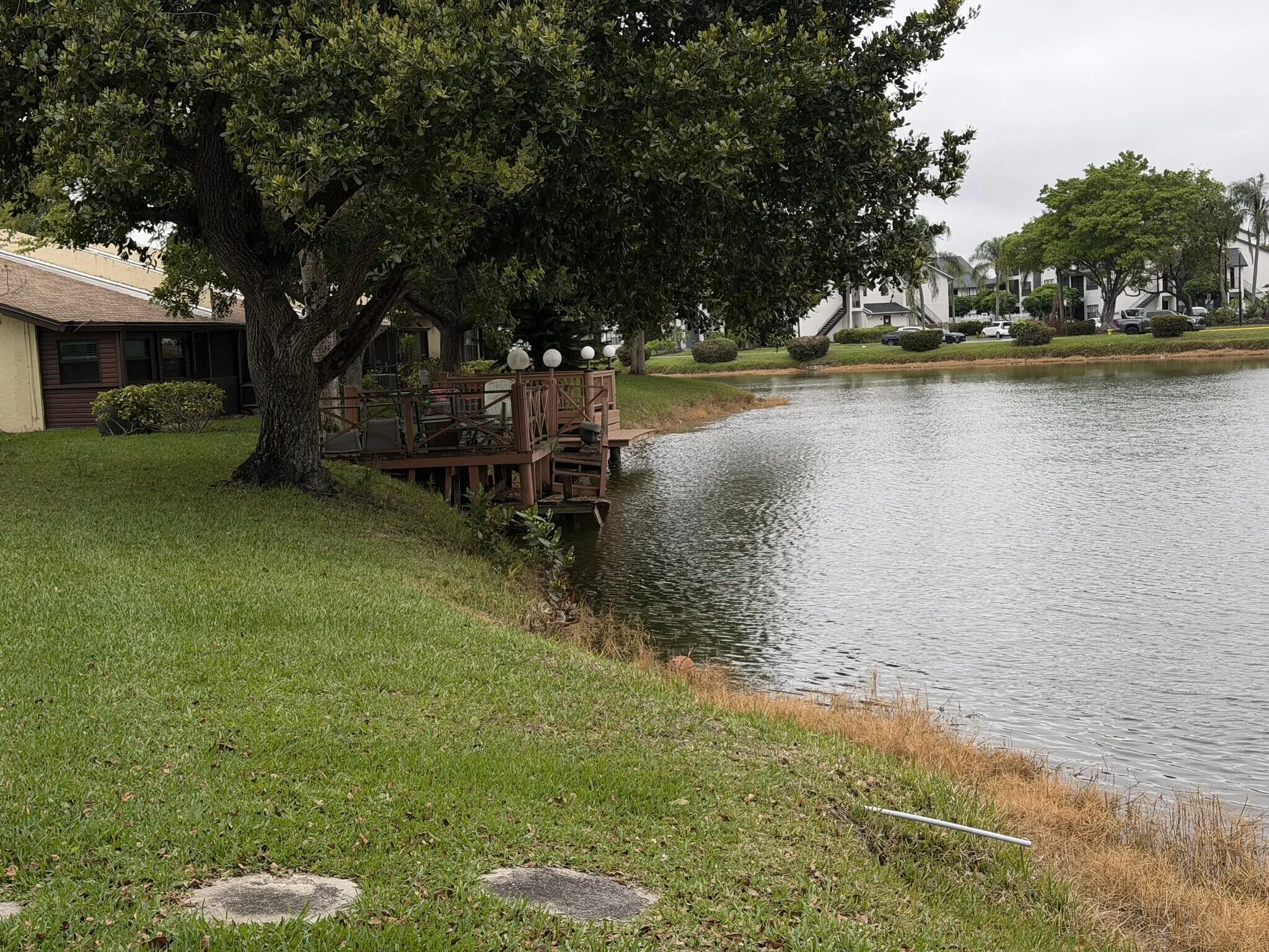 Waterfront property featuring a wood-finish deck with railing, mature trees, and a manicured lawn