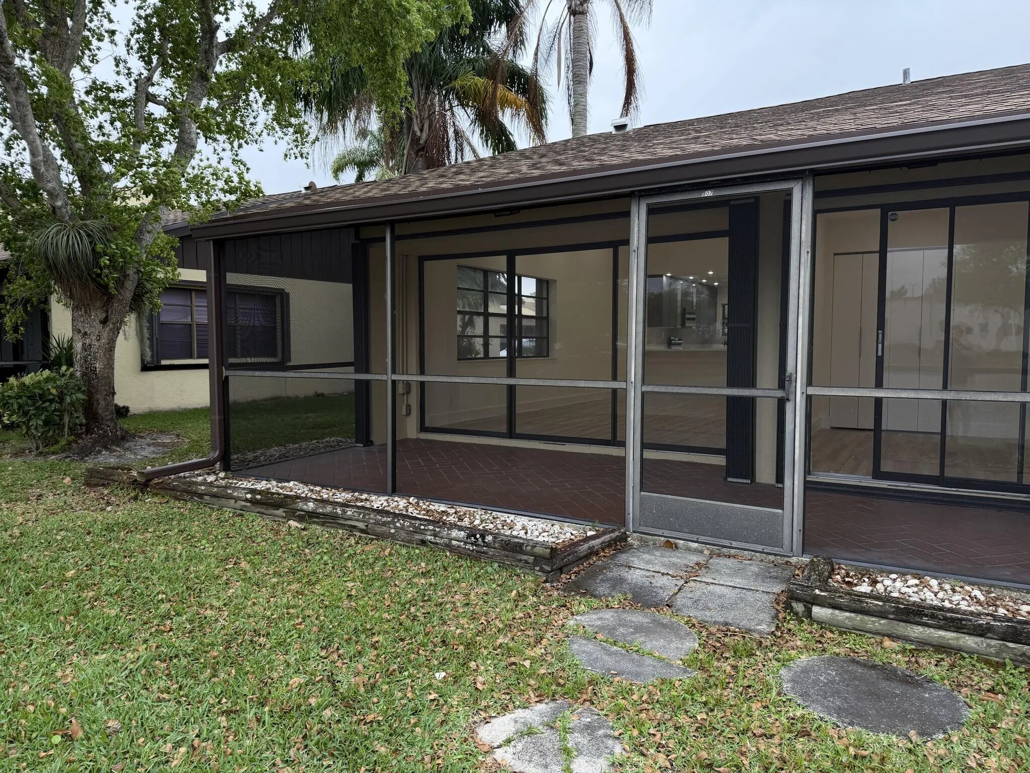 Screened patio with a dark finish floor, multiple sliding glass doors, and a partial outdoor rock bed