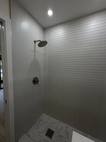 Recessed ceiling lighting, rain shower head, brushed nickel fixtures, horizontal textured wall tiling, and mosaic tile flooring