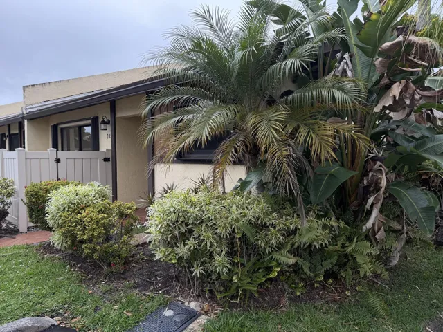 Lush tropical landscaping, light-colored exterior, privacy fence, exterior lighting fixture, and dark-framed windows