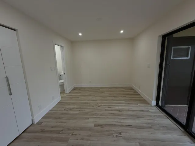 Wood-finish flooring with white baseboards, recessed lighting, and a sliding glass door