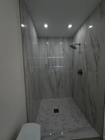 Walk-in shower featuring large format wall tiles, a mosaic tile floor, and a built-in recessed niche