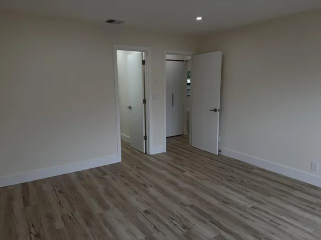 Wood-finish flooring throughout, bright white walls, recessed ceiling lighting, and white baseboards
