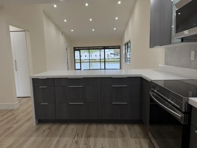 Kitchen featuring wood-finish flooring, dark wood-grain cabinetry, light countertops, a built-in microwave, and a glass cooktop