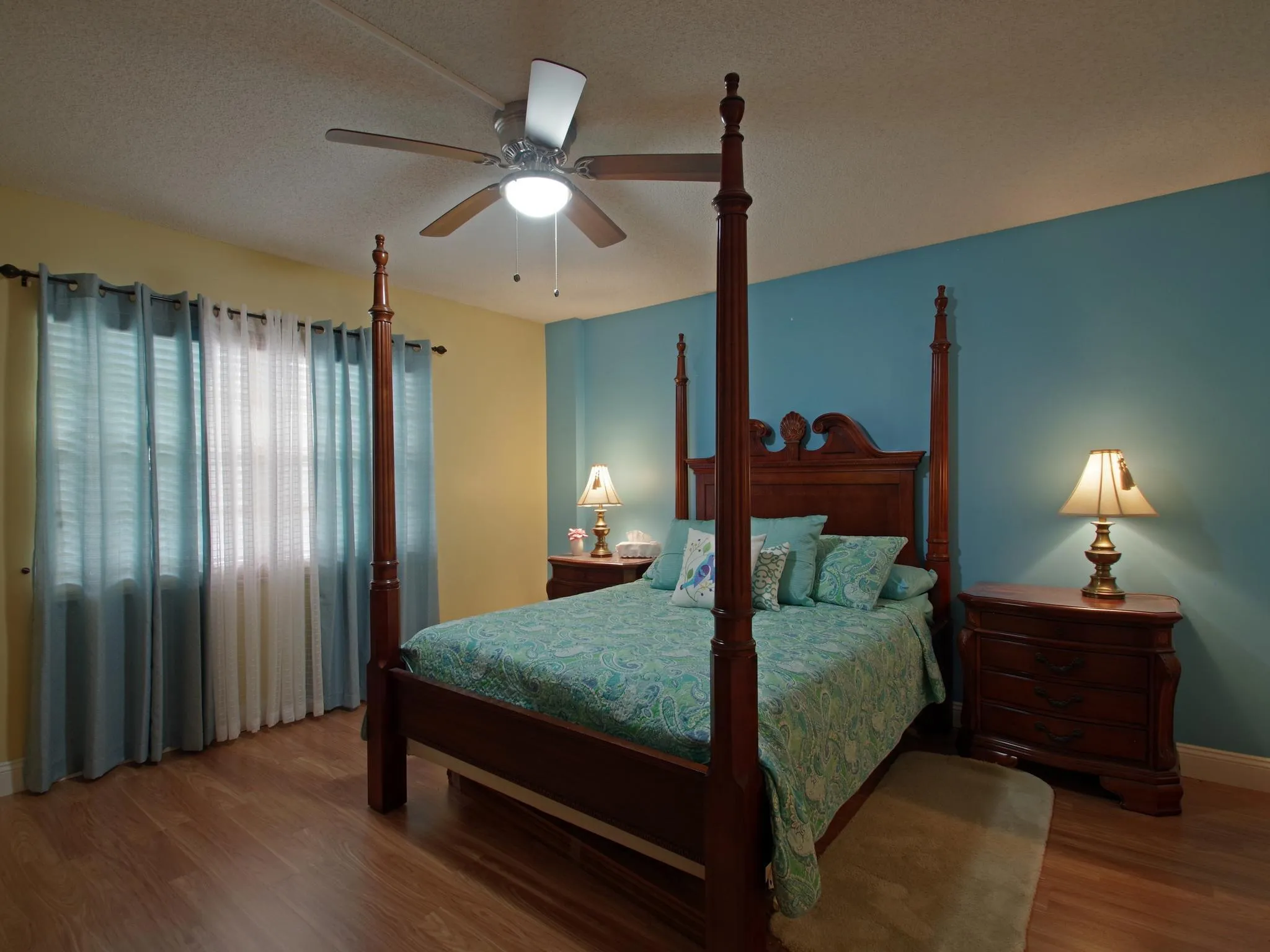 Wood-finish flooring, ceiling fan with integrated lighting, window with drapes, and painted walls